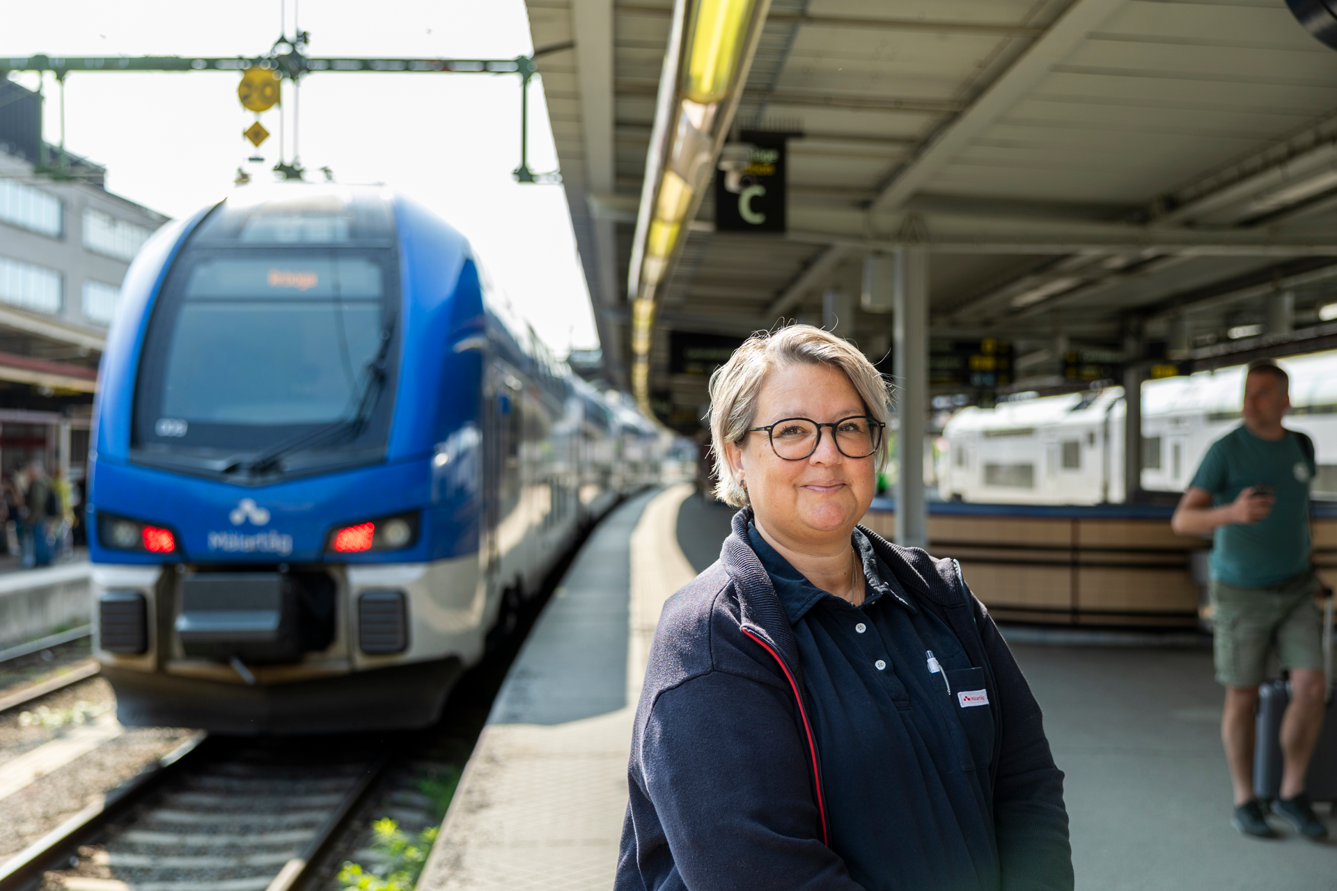 A female train attendant standing in front of a train at a train station