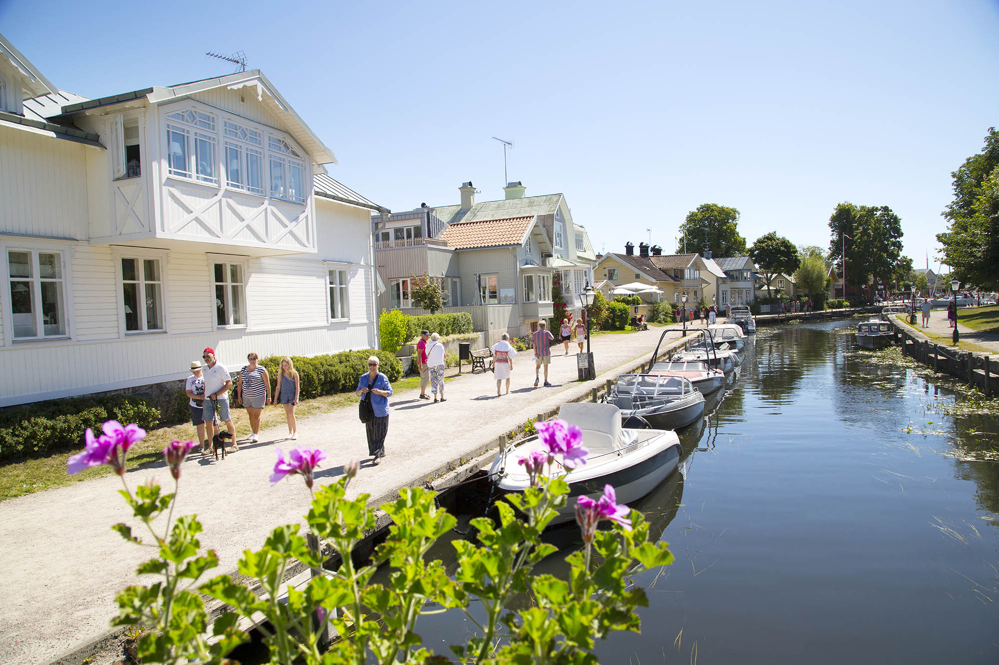 Människor promenerar i solen längs en å som rinner genom Trosa