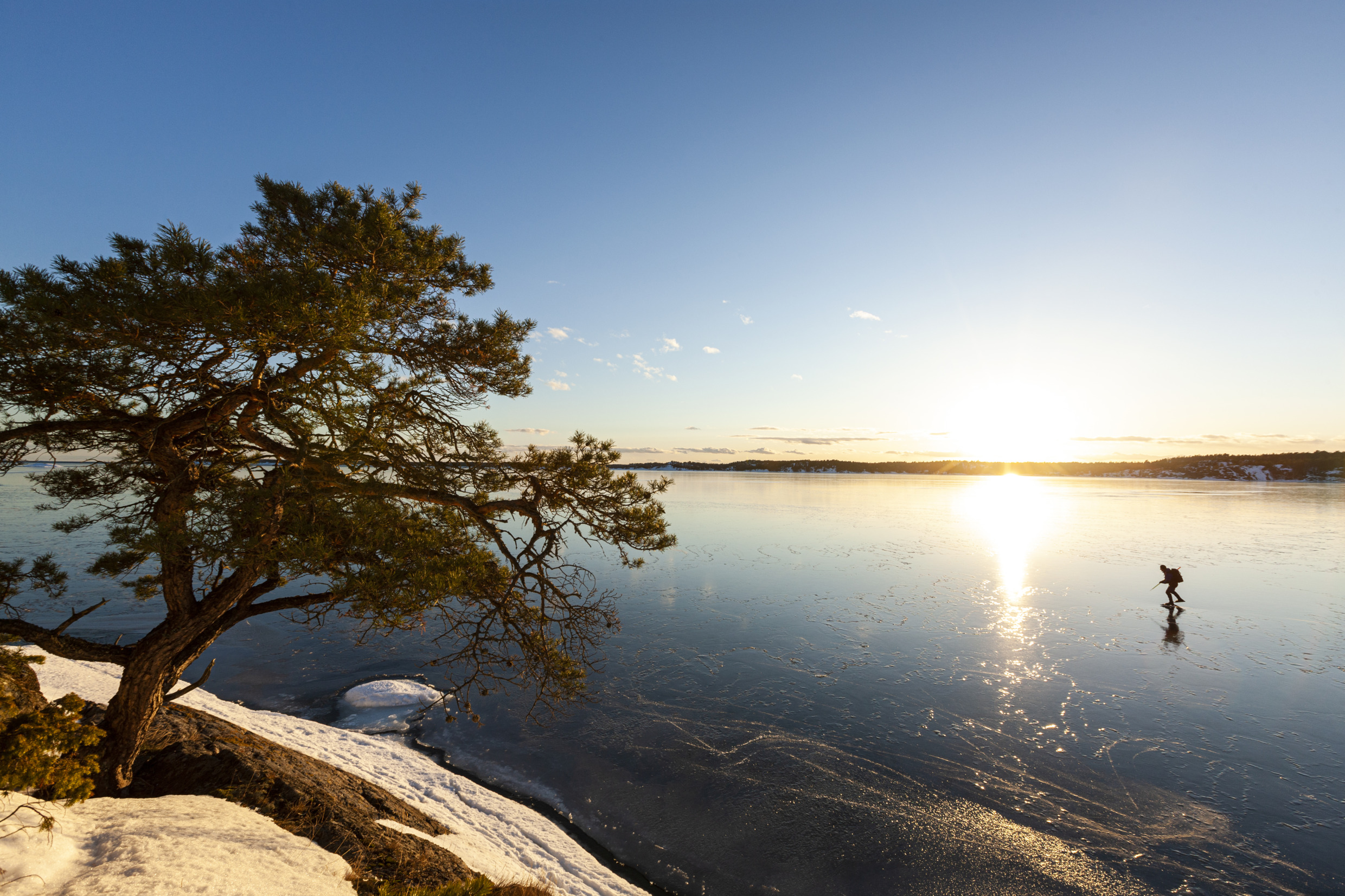 En istäckt sjö vid soluppgång med en ensam långfärdsskriskoåkare