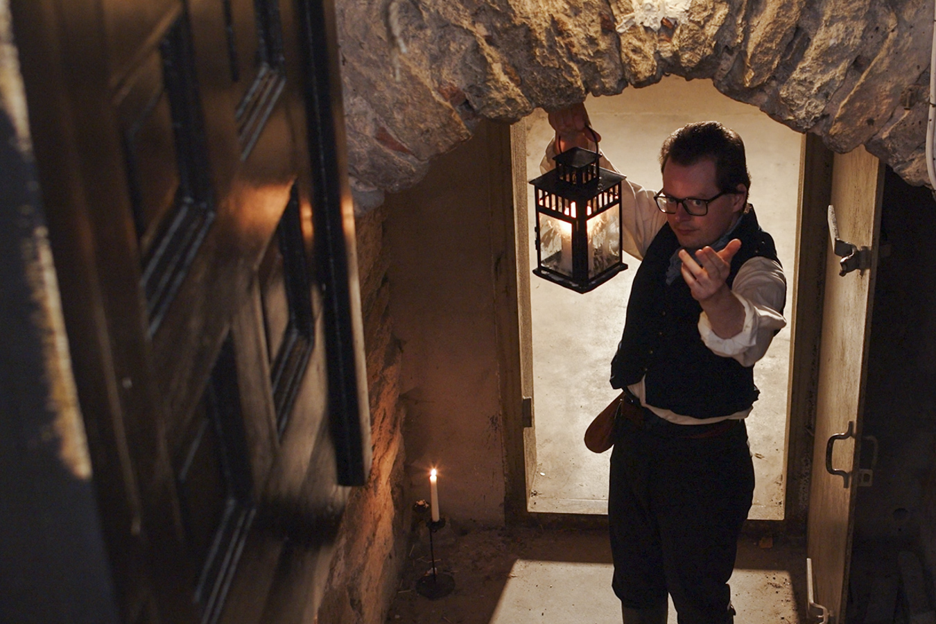 En man med en lykta som vinkar in till en källaringång.