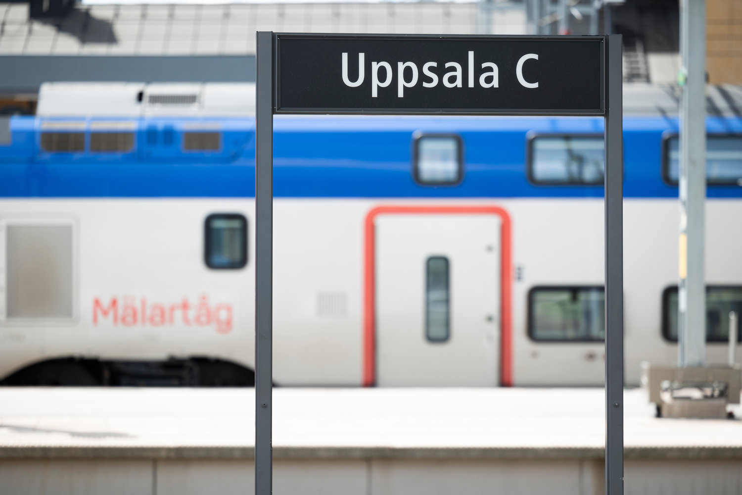 En skylt där det står Uppsala med ett Mälartåg i bakgrund