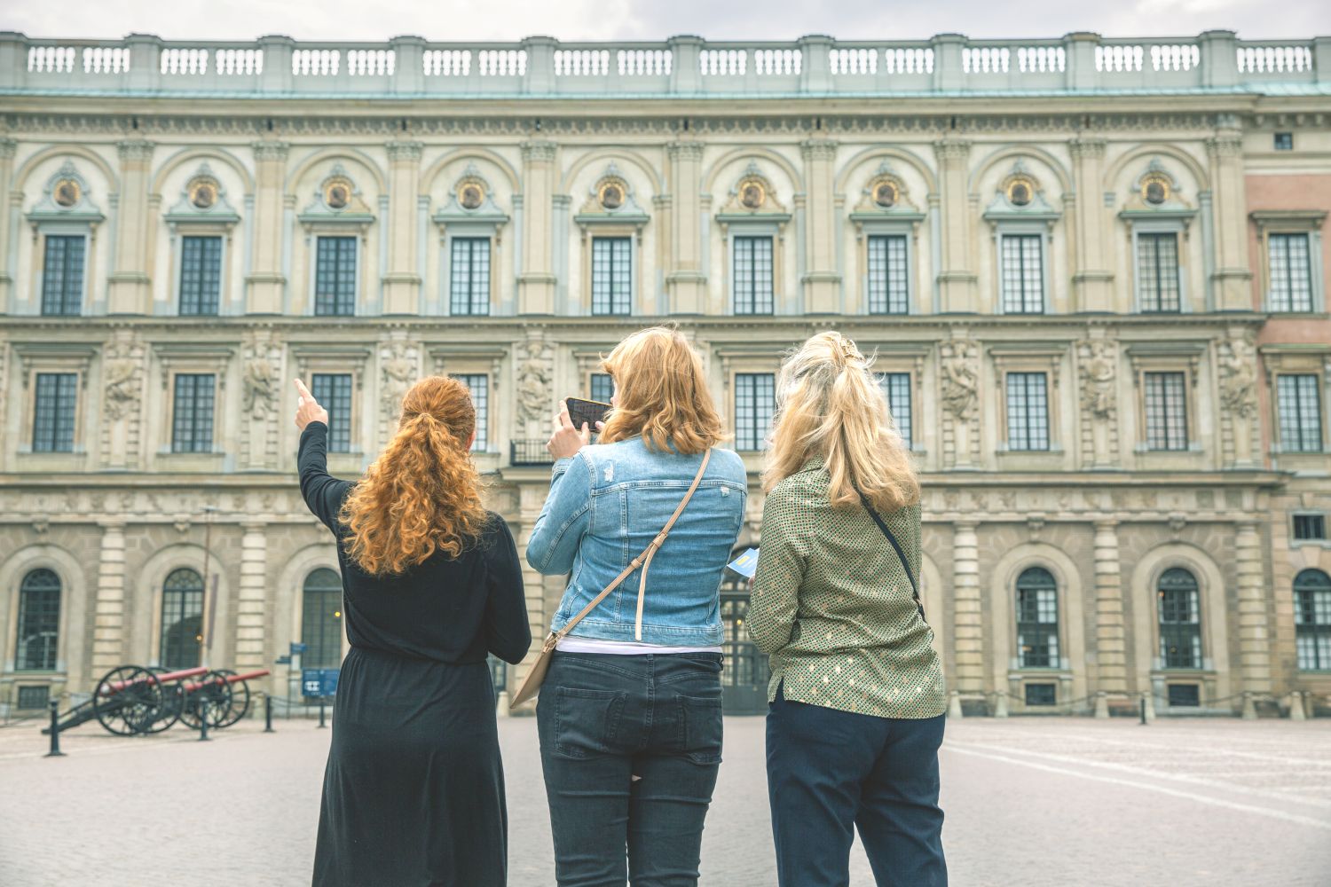 Tre kvinnor står med ryggen mot kameran och tittar på fasaden till Kungliga slottet. 