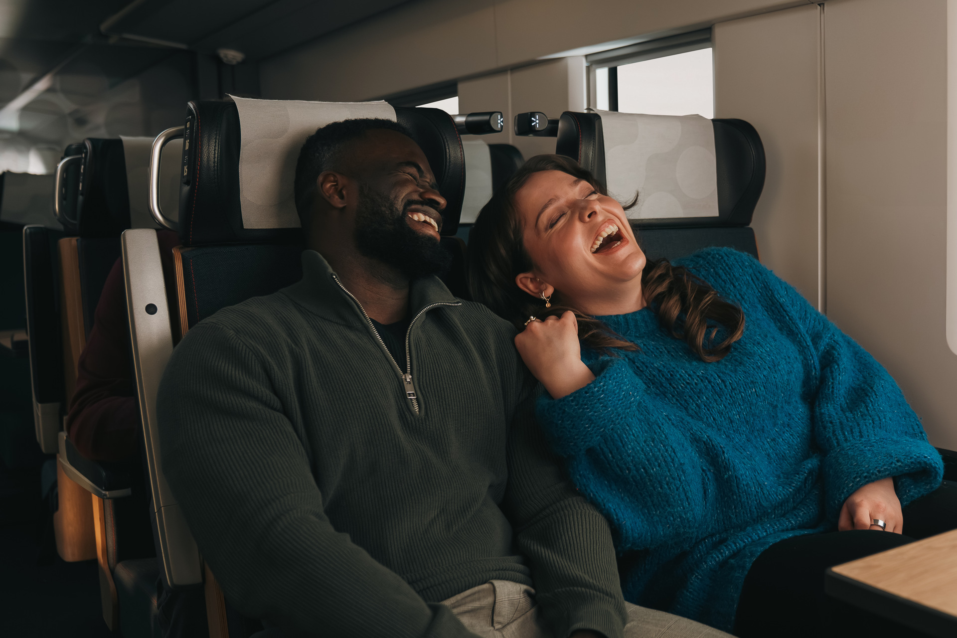 A man and a woman sitting at the windowseat in the train laughing.